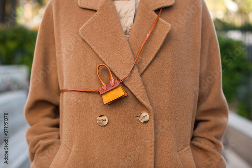 Fashionable young woman wearing beige wool coat. She is holding trendy mini bag in hands. Street style.  photo