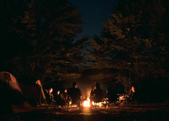 The group of young people are sitting around the bonfire and talking and singing songs