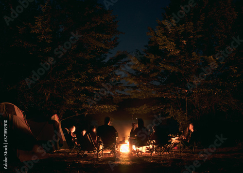 The group of young people are sitting around the bonfire and talking and singing songs