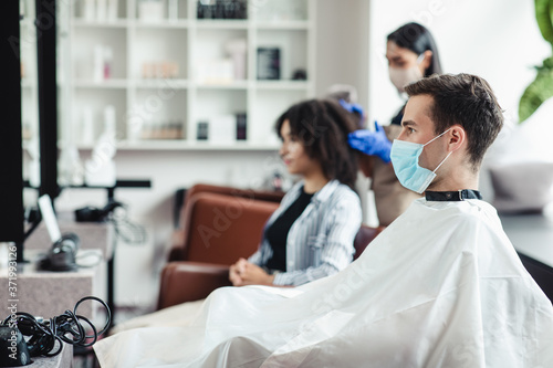 Man in medical mask sitting at hairdressers  waiting for master