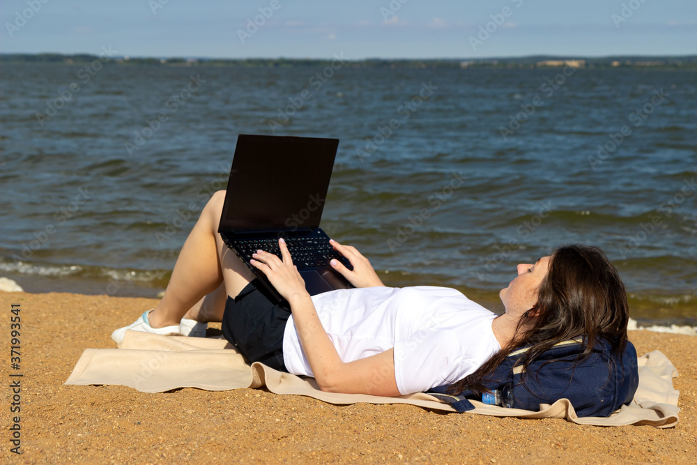 Young woman using laptop computer on a beach. Freelance work concept