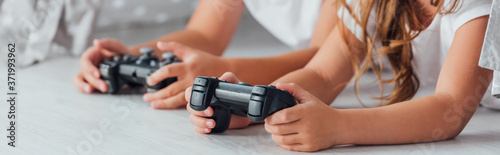 KYIV, UKRAINE - JULY 21, 2020: cropped view of brother and sister lying on floor and playing video game with joysticks, horizontal image © LIGHTFIELD STUDIOS