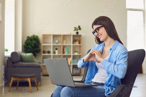 Online dating. Happy young woman talking to her boyfriend on laptop. Loving girl showing heart with hands to pc screen