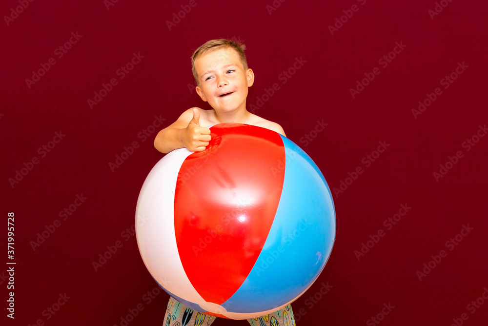 Happy caucasian schoolboy playing inflatable beach ball on red background.concept summer vacation Happy caucasian schoolboy playing inflatable beach ball on red background.concept summer vacation