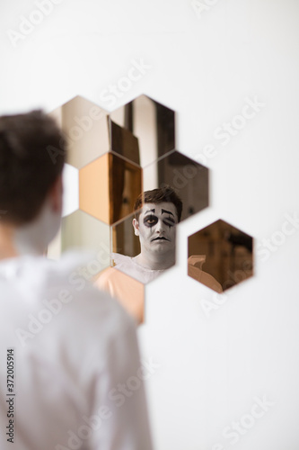 a man in a piero suit looks in the mirror at the halloween party. Happy Halloween. depression. psychology
