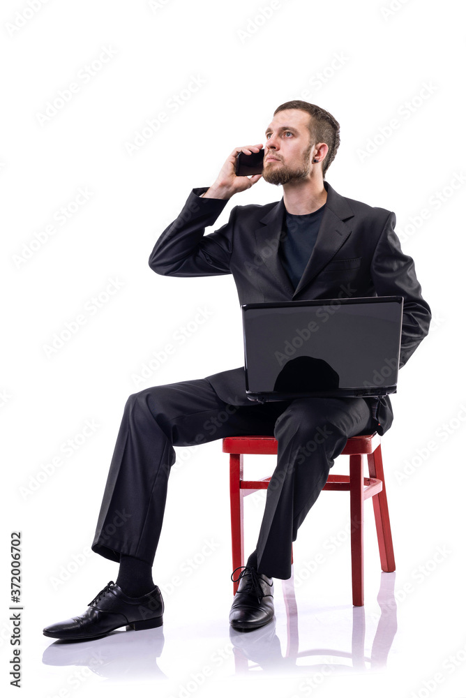 A bearded business man sits on a chair, holds a laptop and talks on the phone, on a white background. A bearded business man sits on a chair, holds a laptop and talks on the phone, on a white background.