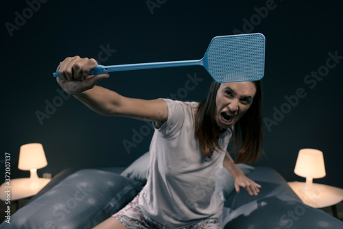 Angry woman killing mosquitoes with a fly swatter photo