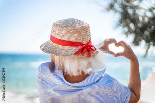 Blonde girl in a straw hat with her back makes love sign with her hands on blue sea background