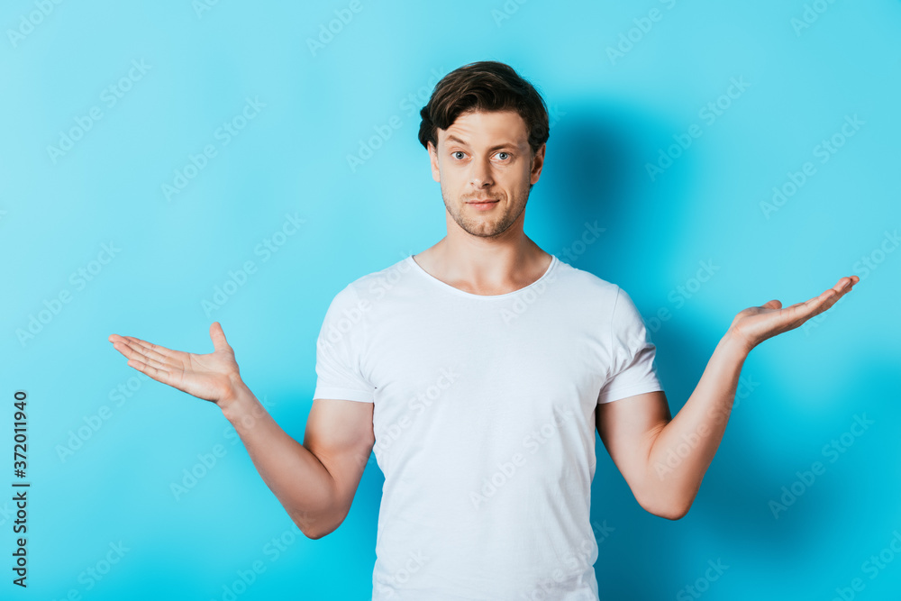 Confused man in white t-shirt pointing with hands on blue background Confused man in white t-shirt pointing with hands on blue background