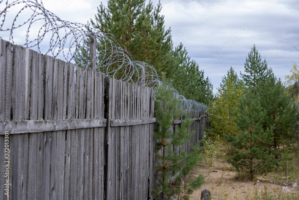 Wooden fence with barbed wire on the background of the cloudy sky.