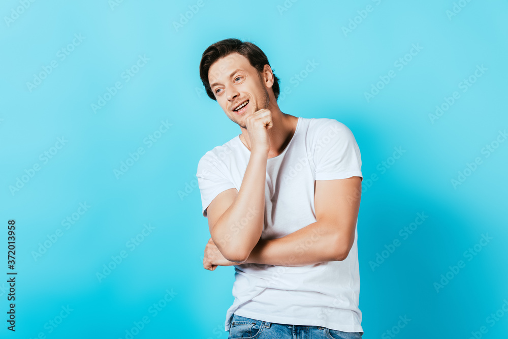 Young man with fist near chin looking away on blue background
