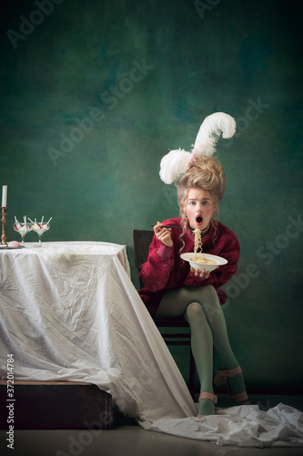 Instant noodles. Young woman as Marie Antoinette isolated on dark green background. Retro style, comparison of eras concept. Beautiful female model like classic historical character, old-fashioned. © master1305