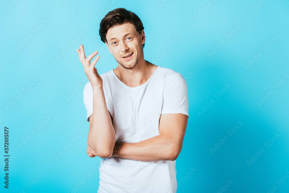 Young man in white t-shirt gesturing and looking at camera on blue background Young man in white t-shirt gesturing and looking at camera on blue background