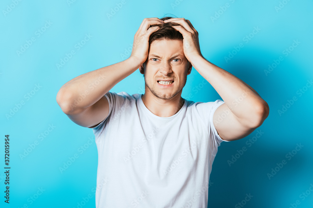 Young angry man in white t-shirt looking at camera on blue background Young angry man in white t-shirt looking at camera on blue background