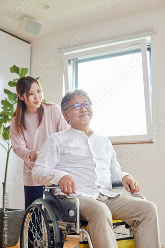 車椅子のシニアの男性を介助する若い女性