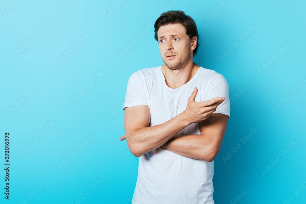 Confused man pointing with hand while looking away on blue background Confused man pointing with hand while looking away on blue background