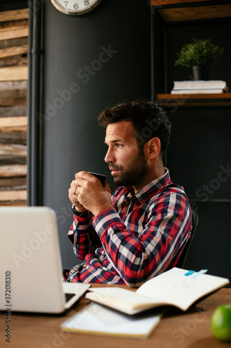 Young businessman drinking coffee in office. Businessman sitting at office desk working on laptop computer...
