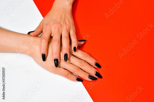 Stylish trendy female black manicure. Beautiful old woman s hands on white and red background