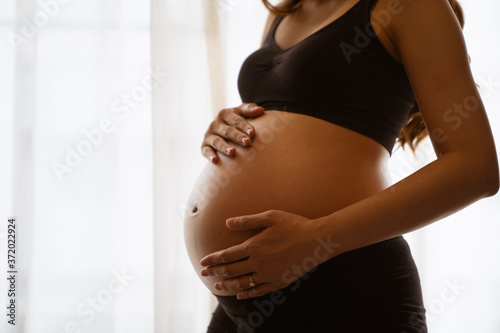Close-up of a pregnant woman touching her belly on the foreground in emotional smile happy by asian woman