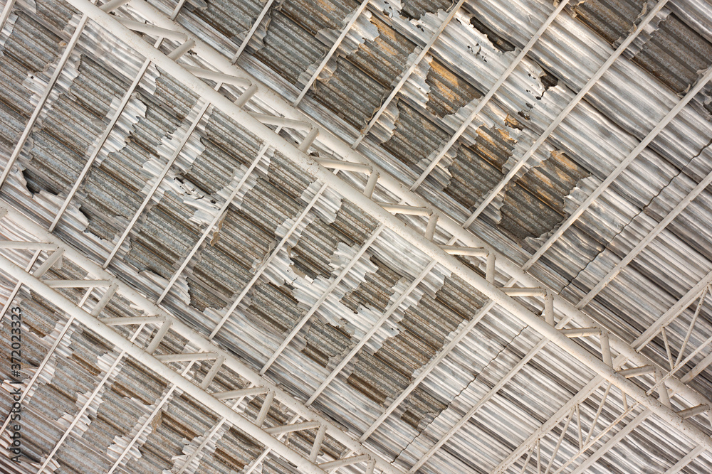 The angle of elevation of old and damaged insulation sheet peels off from the metal sheet roof that installed on metal structure The angle of elevation of old and damaged insulation sheet peels off from the metal sheet roof that installed on metal structure