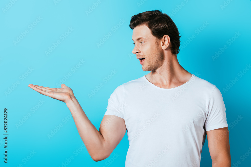 Man in white t-shirt pointing with hand on blue background Man in white t-shirt pointing with hand on blue background
