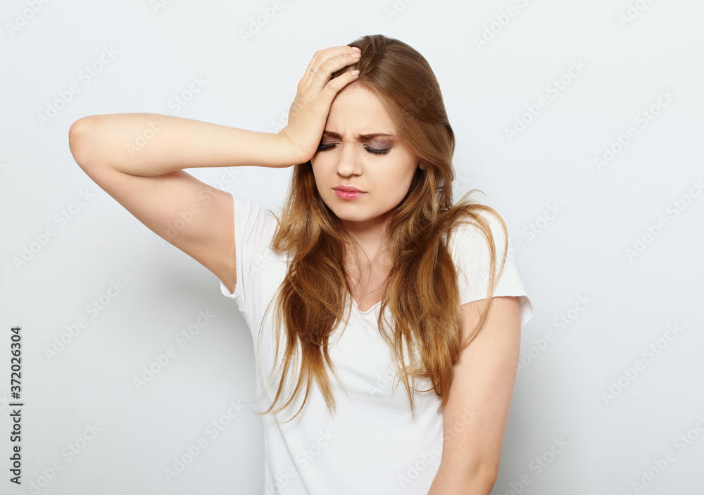Beautiful angry unhappy thinking woman holding the hand with headache and raised eyebrow on blue background. Closeup portrait Beautiful angry unhappy thinking woman holding the hand with headache and raised eyebrow on blue background. Closeup portrait