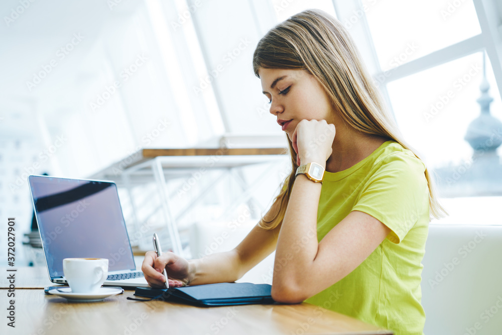 Smart student with writing down homework in notebook sitting in coworking space with coffee.Pensive female recording checklist in diary sitting in university at laptop computer with mock up area Smart student with writing down homework in notebook sitting in coworking space with coffee.Pensive female recording checklist in diary sitting in university at laptop computer with mock up area