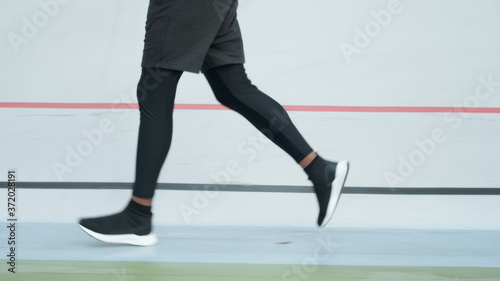 Male jogger training at stadium track. Athlete legs running on racetrack