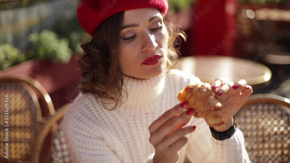 Beautiful woman in red beret sitting outside and eating croissant . French style Beautiful woman in red beret sitting outside and eating croissant . French style