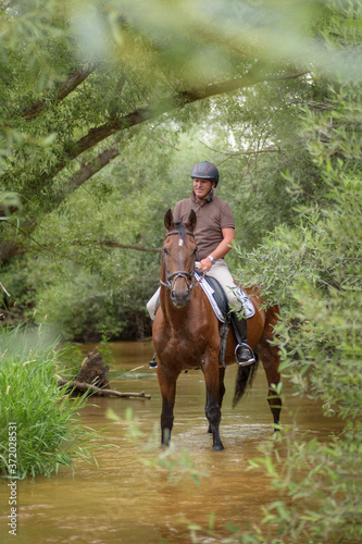 Man riding a horse in the river with green vegetation environment. Horse riding in the open air.