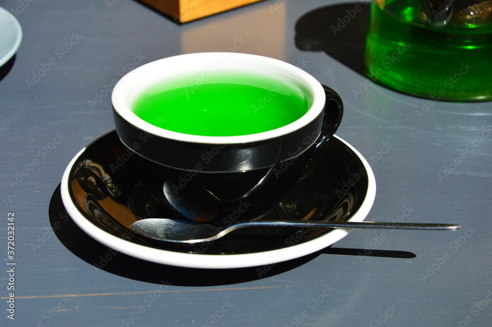 green tea in a black Cup. a teaspoon and a mug on the gray table. bright color. green tea in a black Cup. a teaspoon and a mug on the gray table. bright color.