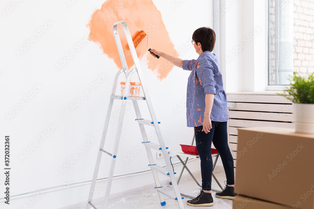 Happy middle-aged woman painting wall in her new apartment. Renovation, redecoration and repair concept.