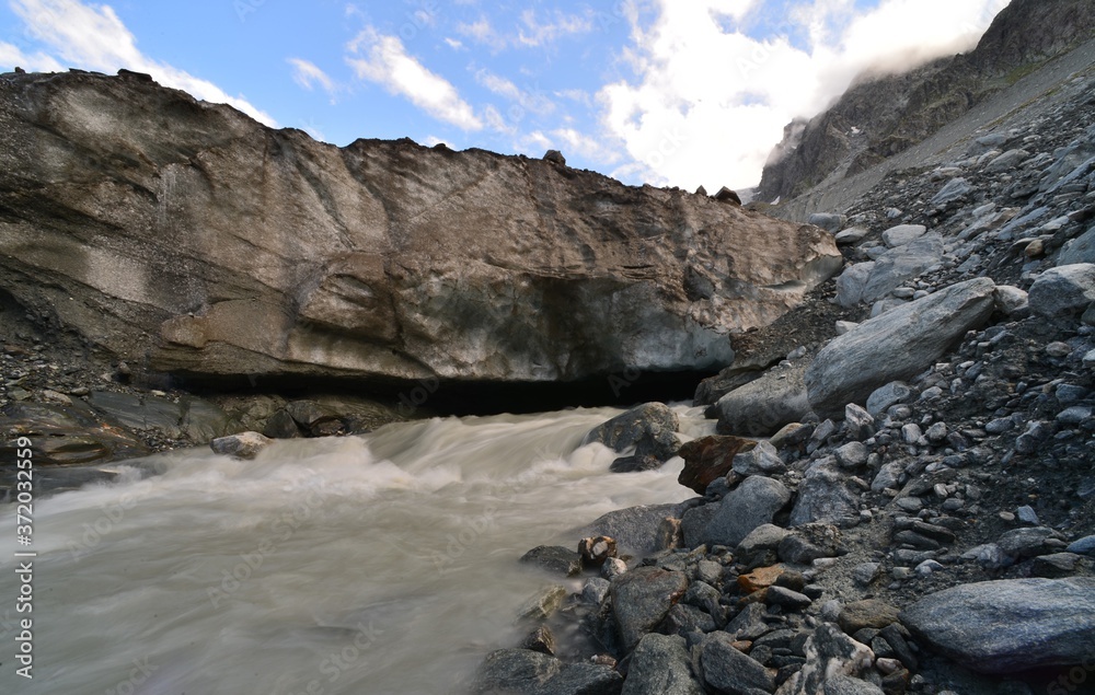 Glacier river from a glacier cave in the alps in valais in switzerland with a bright blue sky Glacier river from a glacier cave in the alps in valais in switzerland with a bright blue sky