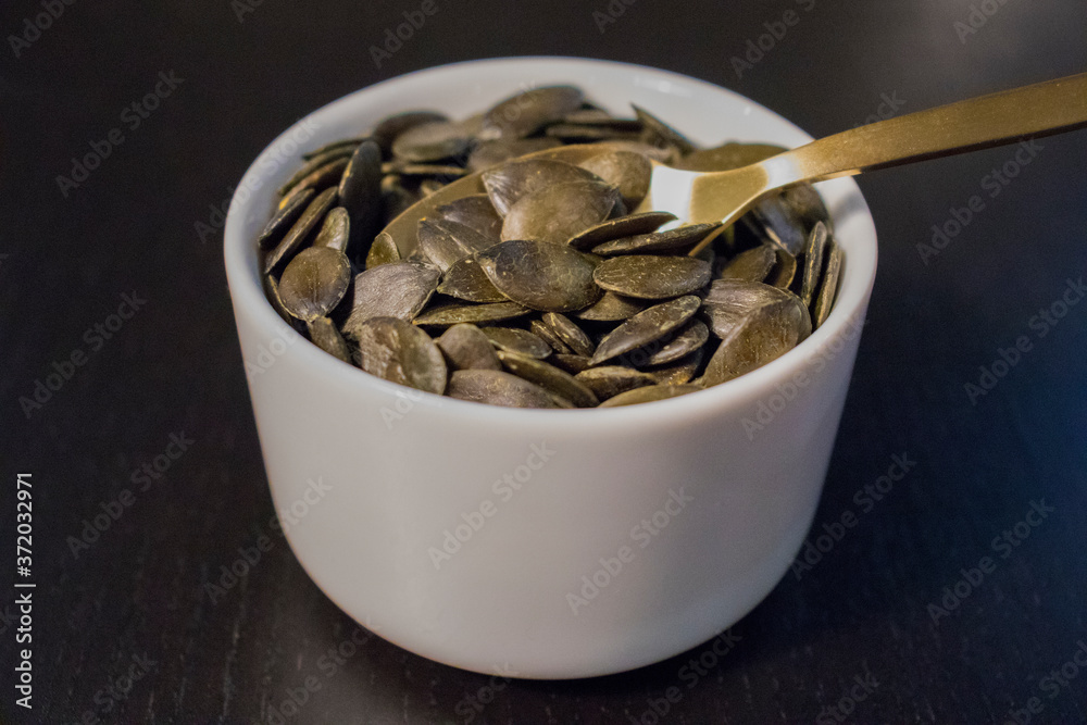 Raw pumpkin seeds and spoon in white bowl on black table. Raw pumpkin seeds and spoon in white bowl on black table.