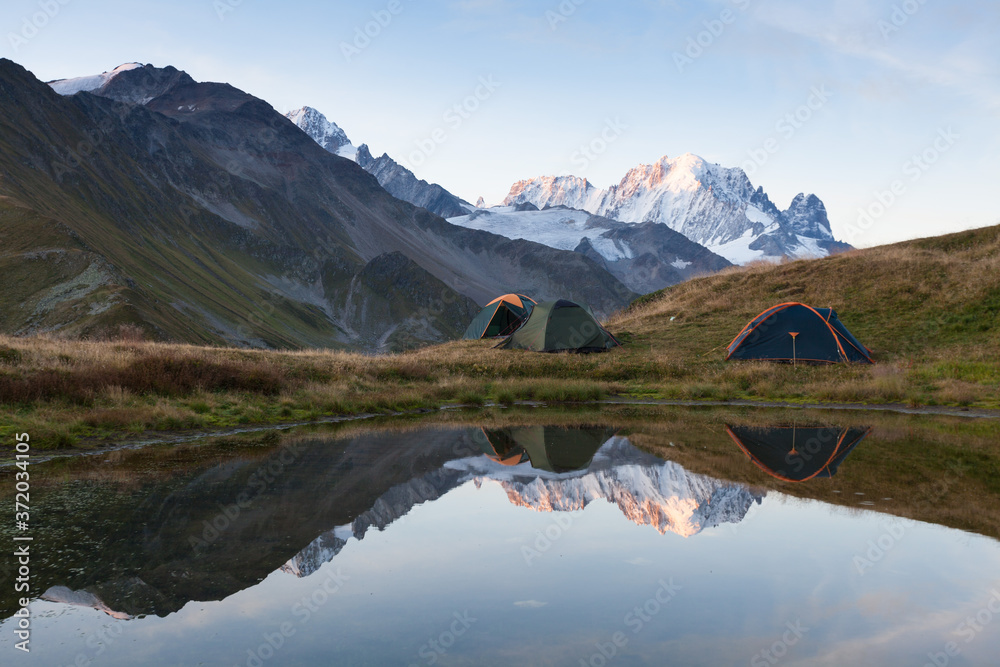 Green tent in the mountains during a colorful sunset. Night bivouac, million star hotel under night sky, tent on pass in Alps. Camping in the high mountains. - obrazy, fototapety, plakaty 