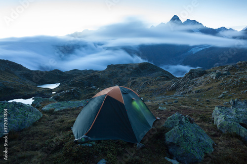 Green tent in the mountains during a colorful sunset. Night bivouac, million star hotel under night sky, tent on pass in Alps. Camping in the high mountains.