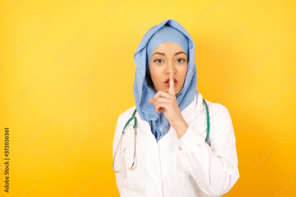 Young arab doctor woman wearing medical uniform standing over yellow background asking to be quiet with finger on lips. Silence and secret concept. Young arab doctor woman wearing medical uniform standing over yellow background asking to be quiet with finger on lips. Silence and secret concept.
