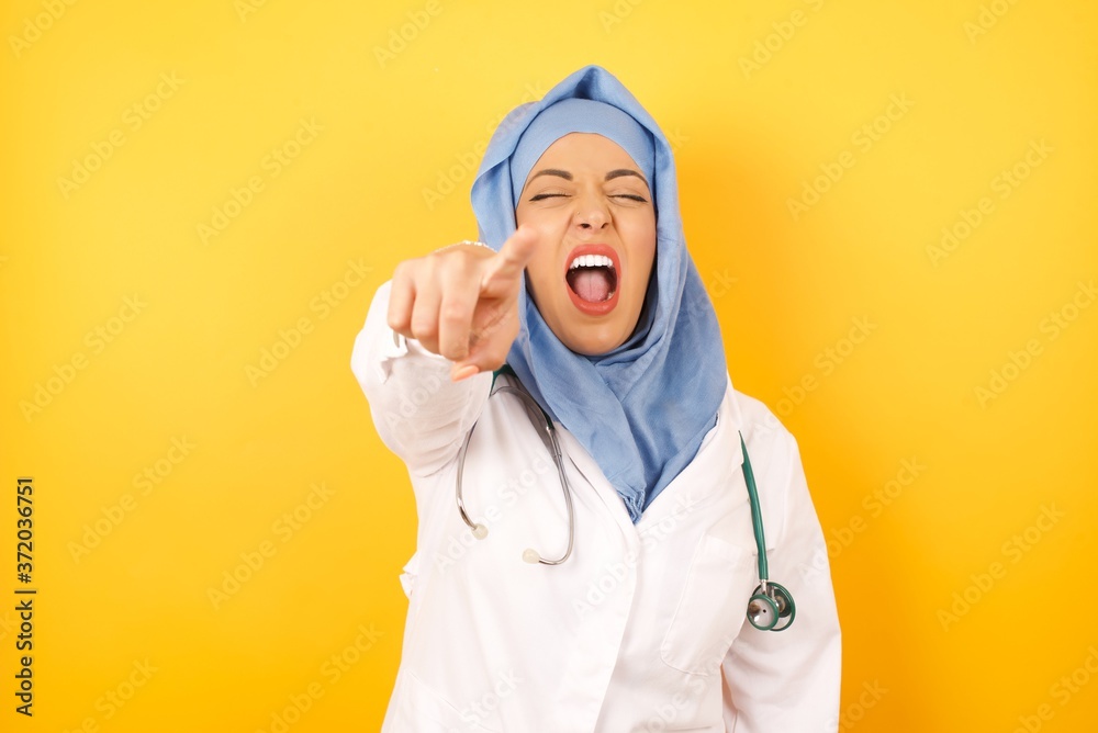 Φωτογραφία Young arab doctor woman wearing medical uniform standing over yellow background  pointing displeased and frustrated to the camera, angry and furious ready to fight with you