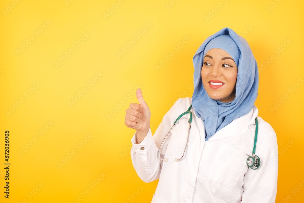 Young arab doctor woman wearing medical uniform, looking proud, smiling doing thumbs up gesture to the side. Good job! Young arab doctor woman wearing medical uniform, looking proud, smiling doing thumbs up gesture to the side. Good job!