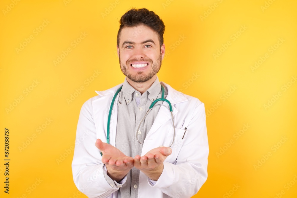 Young Caucasian doctor man wearing medical uniform and stethoscope standing over isolated yellow background Smiling with hands palms together receiving or giving gesture. Hold and protection Young Caucasian doctor man wearing medical uniform and stethoscope standing over isolated yellow background Smiling with hands palms together receiving or giving gesture. Hold and protection