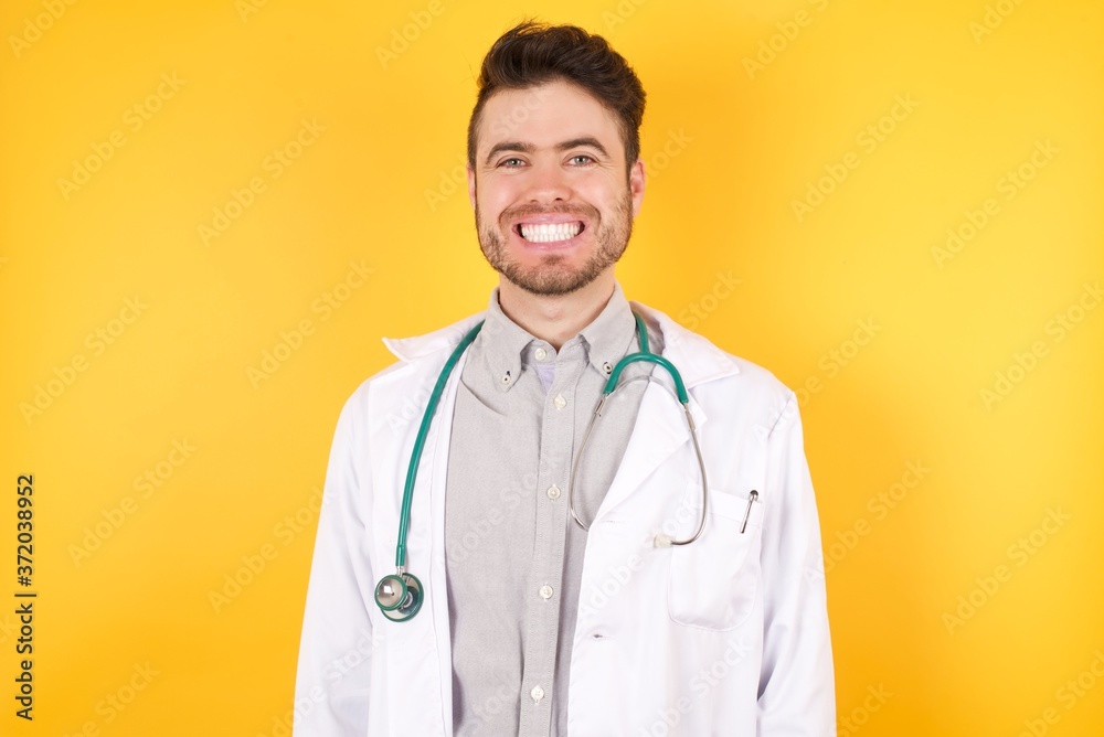 Young Caucasian doctor man wearing medical uniform, over isolated yellow background with a happy and cool smile on face. Lucky person. Young Caucasian doctor man wearing medical uniform, over isolated yellow background with a happy and cool smile on face. Lucky person.