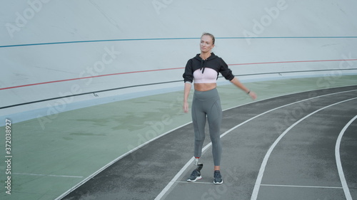 Jogger with artificial limb warming on track. Woman stretching hands at stadium