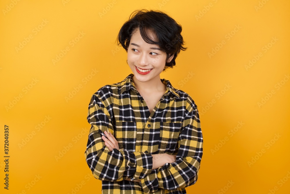 Portrait of dreamy rest relaxed Young asian woman with short hair wearing plaid shirt standing over yellow background crossing arms, looks good Portrait of dreamy rest relaxed Young asian woman with short hair wearing plaid shirt standing over yellow background crossing arms, looks good