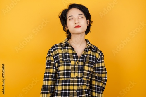 Young asian woman with short hair wearing plaid shirt standing over yellow background looking sleepy and tired, exhausted for fatigue and hangover, lazy eyes in the morning.