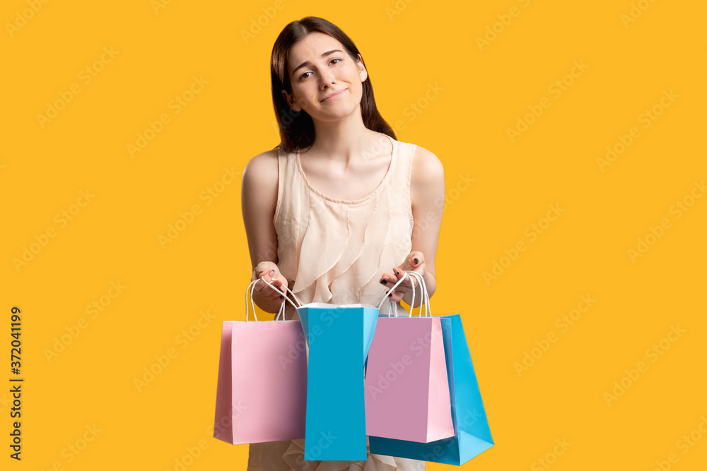 Unpleasant bonus. Online shopping concept. Woman holding colorful bags. Isolated on orange. Shopaholic lifestyle. Sales and discounts