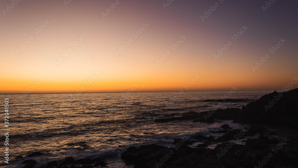 Fototapeta premium Hermoso atardecer en el borde costero de las playas de Punta Tralca en Chile.Puesta de sol en el océano.Cielo despejado con hermosos tonos anaranjados y violeta.