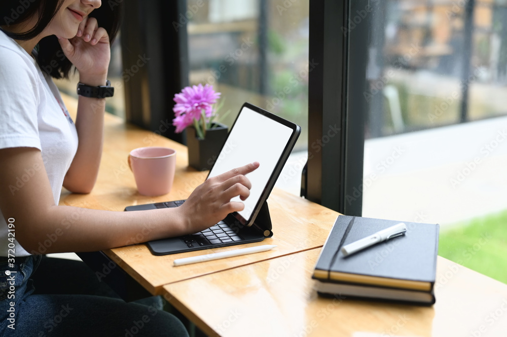 A beautiful woman is using a computer tablet with a white blank screen while sitting at the wooden counter bar. A beautiful woman is using a computer tablet with a white blank screen while sitting at the wooden counter bar.
