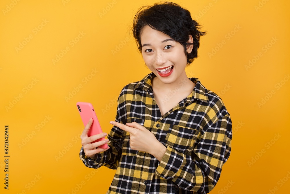 Young beautiful Asian woman wearing plaid shirt over yellow background holding in hands showing new cell, wearing red shirt standing against white background Young beautiful Asian woman wearing plaid shirt over yellow background holding in hands showing new cell, wearing red shirt standing against white background