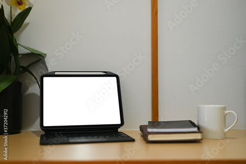 Computer tablet with a white blank screen is putting on a wooden table in the living room.