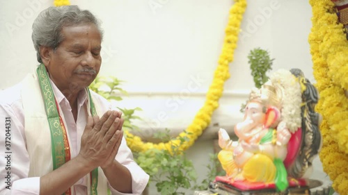 Elder man offering Bhajan in front of Lord Ganesha Idol during Ganesha or vinayaka Chaturthi festvial ceremony at home. photo